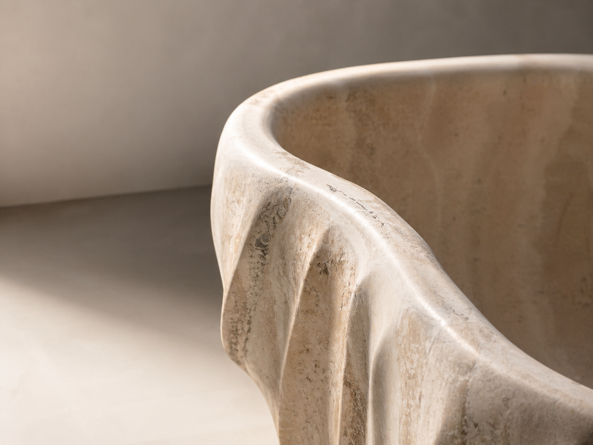Close-up of a sculpted beige stone basin showing its curved rim, inner surface and textured exterior in soft light.