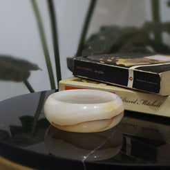 Aura Onyx Ashtray with a vintage round design, placed on a black marble table beside classic books. Elegant home decor and smoking accessory.