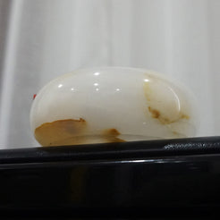 A close-up of the LumiGem Candle Holder against a dark background, showcasing its smooth surface and the unique, glowing quality of the white onyx stone.