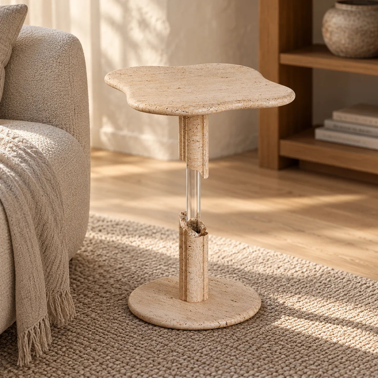 AeroCloud Classico travertine side table with a clear acrylic middle section beside an oatmeal sofa, viewed at a moderate oblique angle.