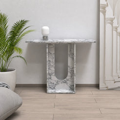 Frontal view of the Alecto Arabescato marble console in a naturally lit living room, with a thin rectangular top and rounded-bottom opening above a continuous stone base.