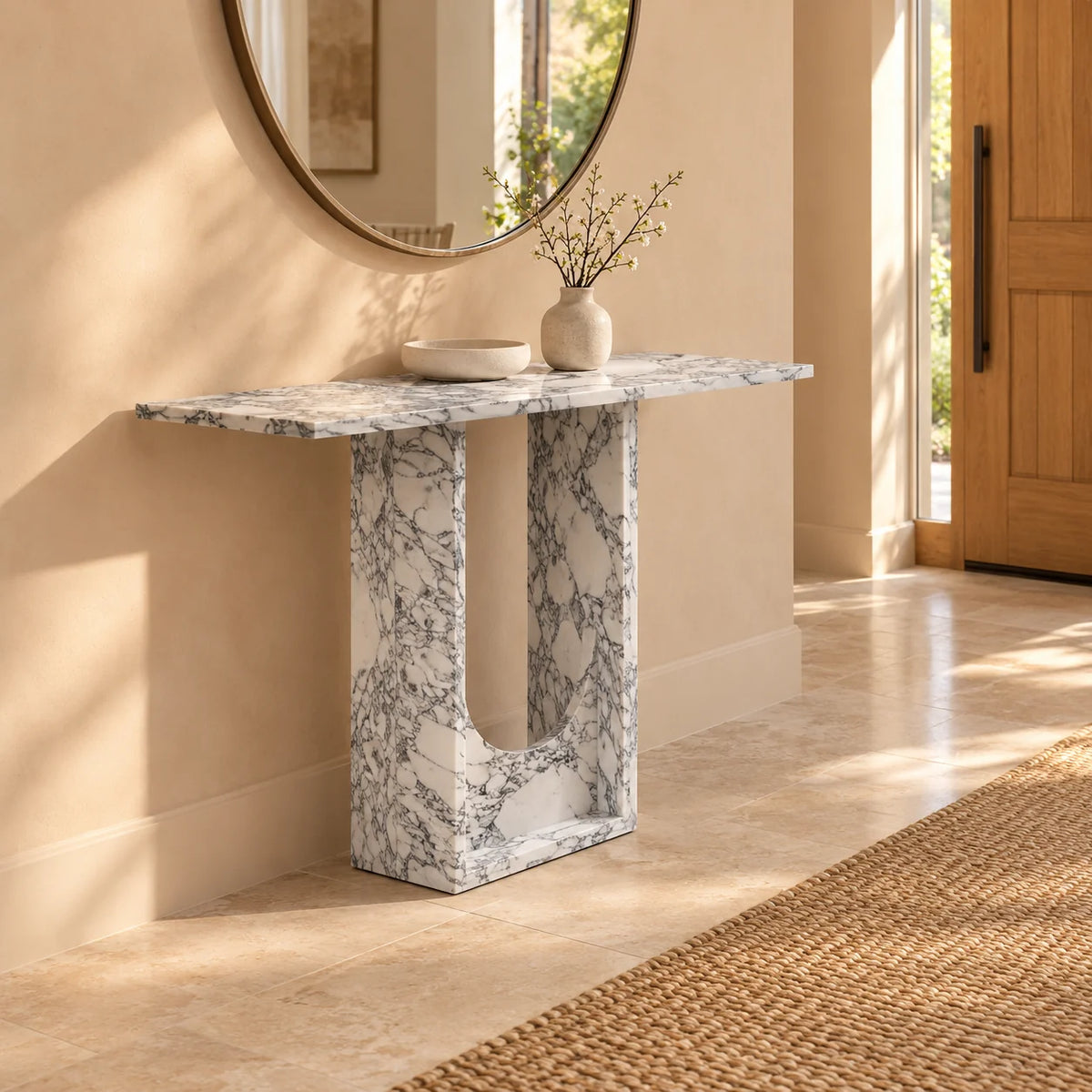 Alecto Arabescato marble console in a warm entrance hall, seen from the left front with its thin rectangular top, deep stone base and rounded-bottom opening.