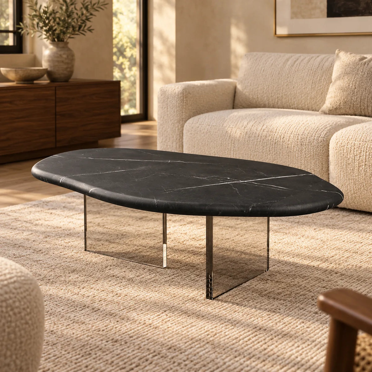 AquaFlow Black Marquina marble coffee table with clear acrylic bases in a warm living room, viewed from a front oblique angle.