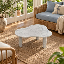 Elevated view of a single CloudDream Italian Carrara marble coffee table in a garden-facing sunroom, showing its cloud-shaped top and three cylindrical supports.