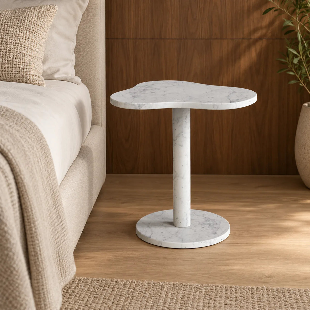 CloudDream Carrara marble side table shown from a low angle beside a linen-covered bed.
