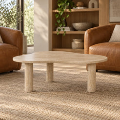 Low front view of the CloudDream Italian Classico travertine coffee table in a leather-chair reading lounge, showing its thin free-form top and three stone legs.