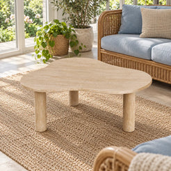 Elevated view of a single CloudDream Italian Classico travertine coffee table in a garden-facing sunroom, showing its cloud-shaped stone top and three cylindrical supports.