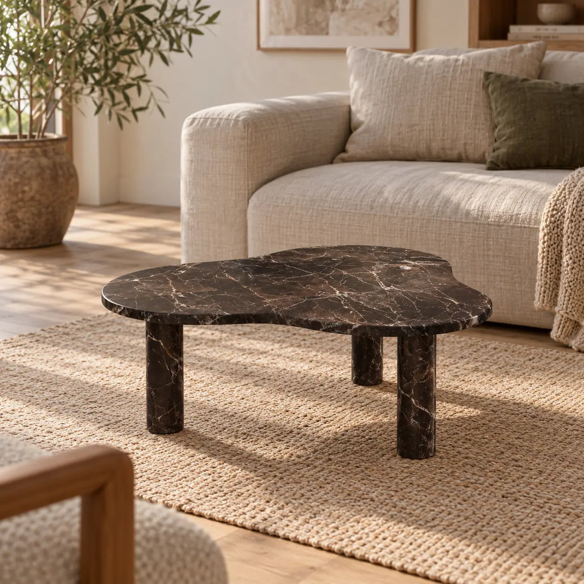 CloudDream Spanish Dark Emperador marble coffee table with a thin cloud-shaped top and three cylindrical legs in a warm linen-sofa living room.