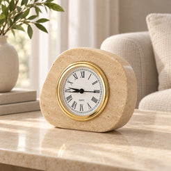Right-side angled view of the beige travertine ZenPebble tabletop clock with a gold-tone Roman numeral dial in a warm neutral interior