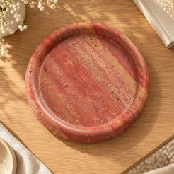 ScarletPebble red travertine round tray, direct overhead view on warm oak