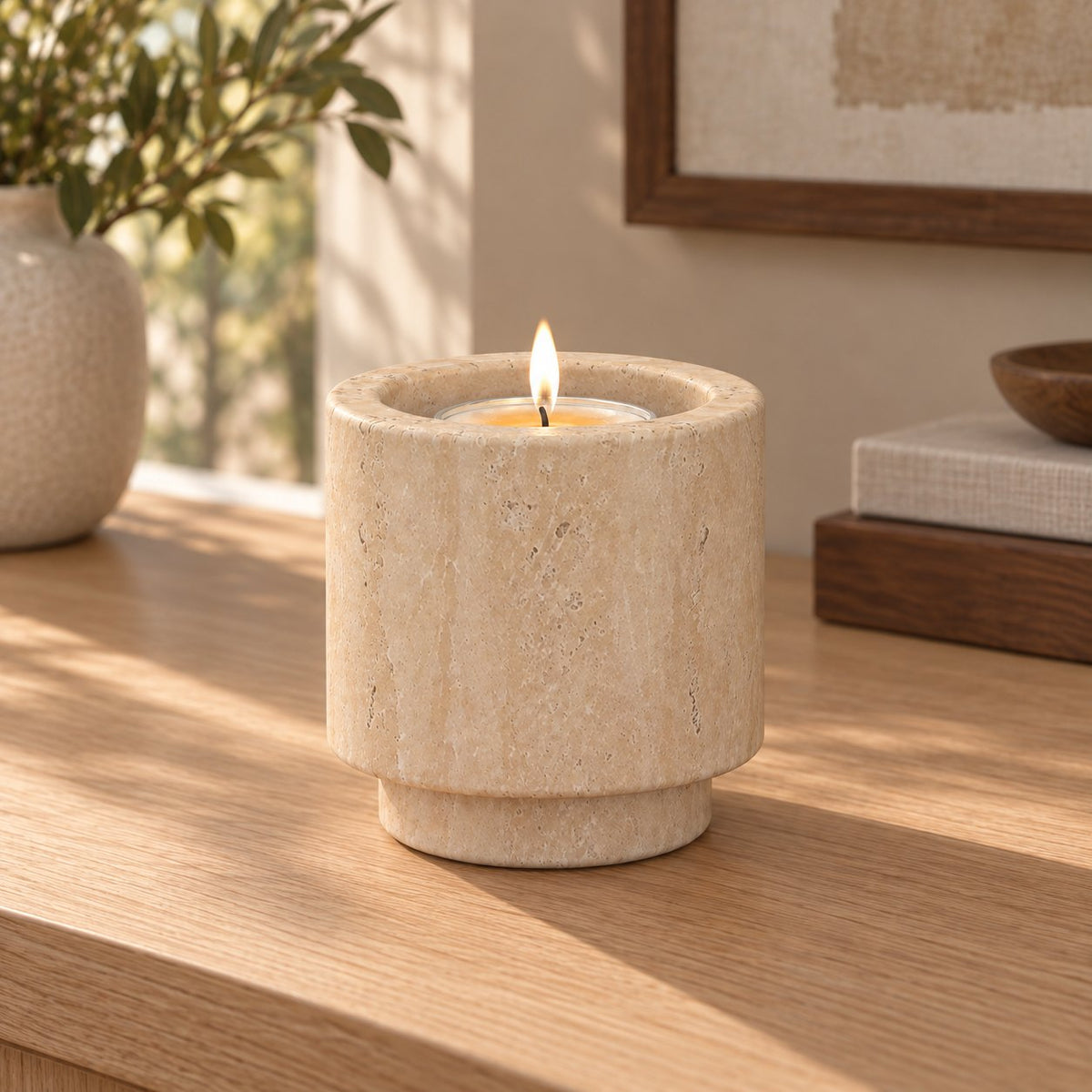 Tall RoundHaven Classico travertine candle holder with one lit tealight, front view in a warm sunlit interior
