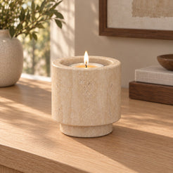 Tall RoundHaven Classico travertine candle holder with one lit tealight, front view in a warm sunlit interior