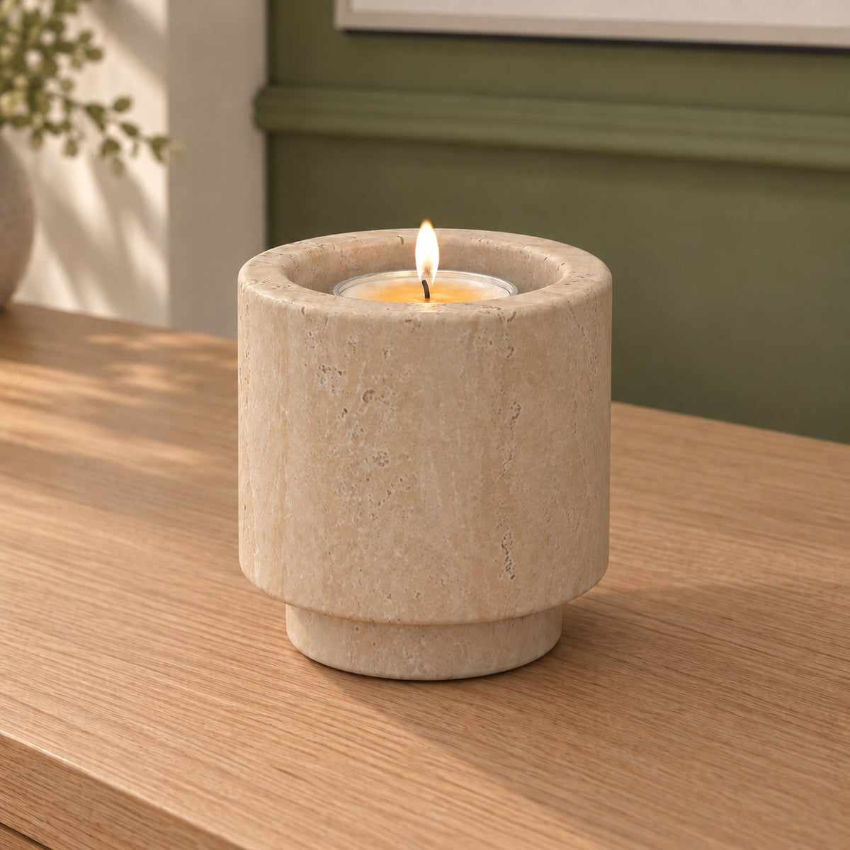 Tall RoundHaven Classico travertine candle holder with a lit tealight, viewed from the right on a warm oak console