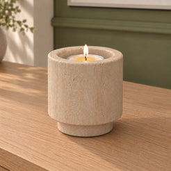 Tall RoundHaven Classico travertine candle holder with a lit tealight, viewed from the right on a warm oak console