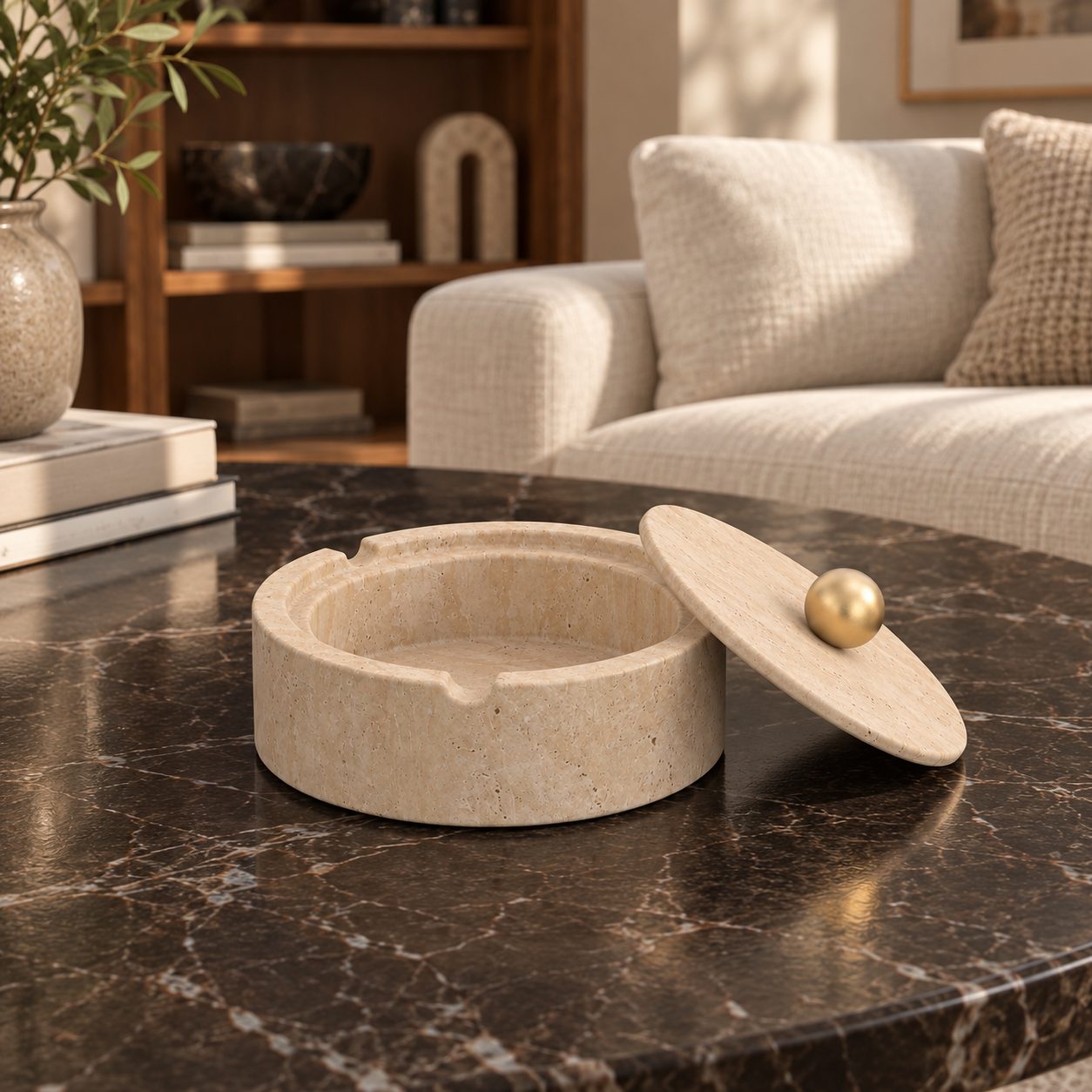 RoundHaven Classico travertine ashtray with one matching gold-knob lid, front view in a warm natural-light interior