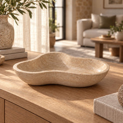 CloudDream Fruit Tray, Italian Classico Travertine, Hero low front oblique camera 15 degrees above tabletop, aligned across wider rim, full rounded outside and shallow interior visible., warm natural light lifestyle