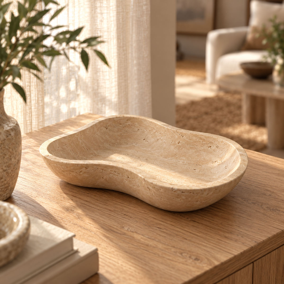 CloudDream Fruit Tray, Italian Classico Travertine, Second angle camera moved to the opposite SIDE of the tray at 45 degrees above tabletop, looking diagonally down so the asymmetric footprint and inner basin are clear; genuinely new camera perspective., warm natural light lifestyle