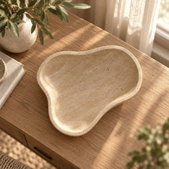 CloudDream Fruit Tray, Italian Classico Travertine, Third angle camera overhead at 85 degrees, tray footprint seen from above with its three unequal organic lobes and shallow rim; still natural lifestyle oak console context., warm natural light lifestyle
