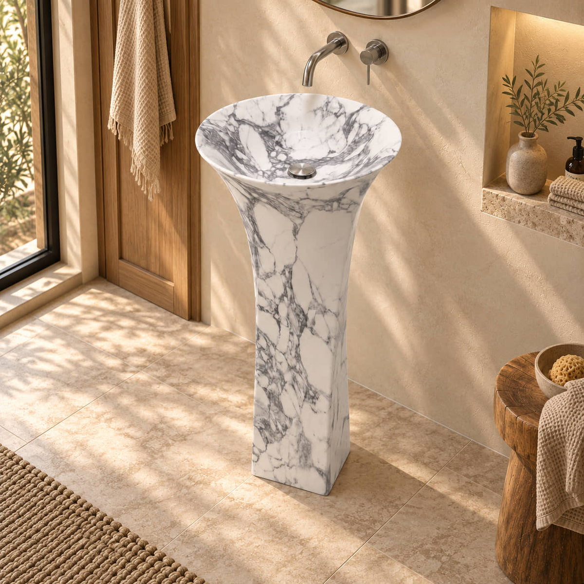 Paka Italian Arabescato Marble Pedestal Sink in a warm cream and oak bathroom, elevated three-quarter view showing the basin, silver drain cover and full square pedestal.