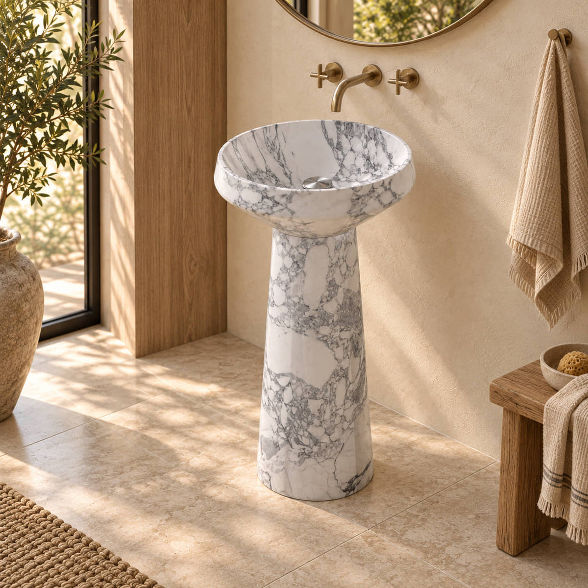 Pala Italian Arabescato Marble Pedestal Sink with a shallow round basin and tapered cylindrical pedestal in a warm cream and natural oak bathroom, three-quarter view.