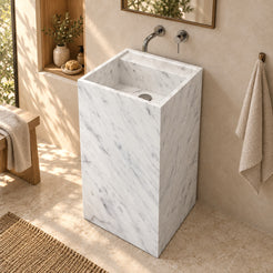 Panini Carrara marble pedestal sink with square basin in a warm ivory and oak bathroom