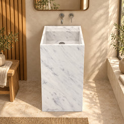 Panini Carrara marble pedestal sink from the front in a warm bathroom with oak wall and natural light
