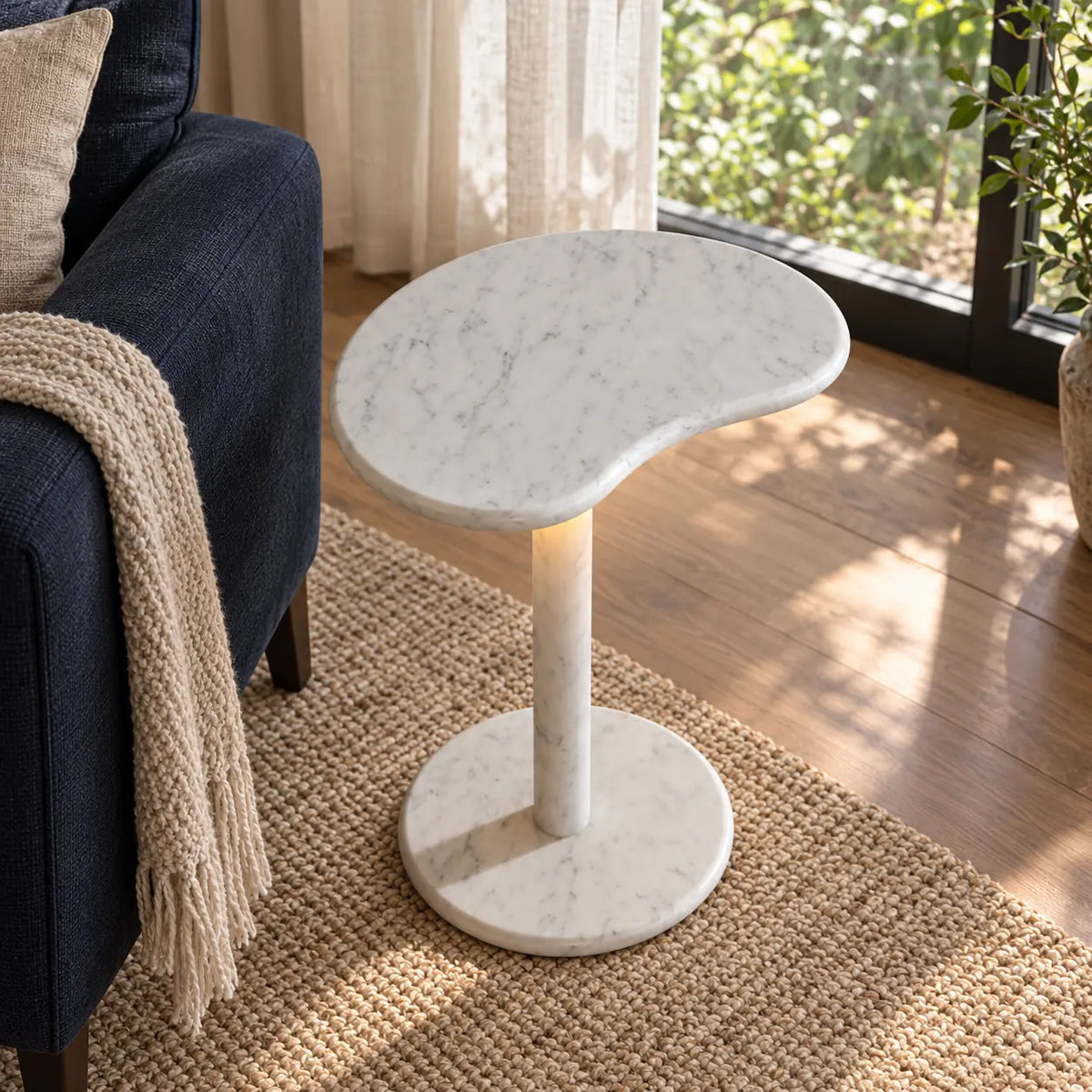 PeaPod Carrara marble smart-edition side table beside a navy reading chair, shown from a high front-quarter view