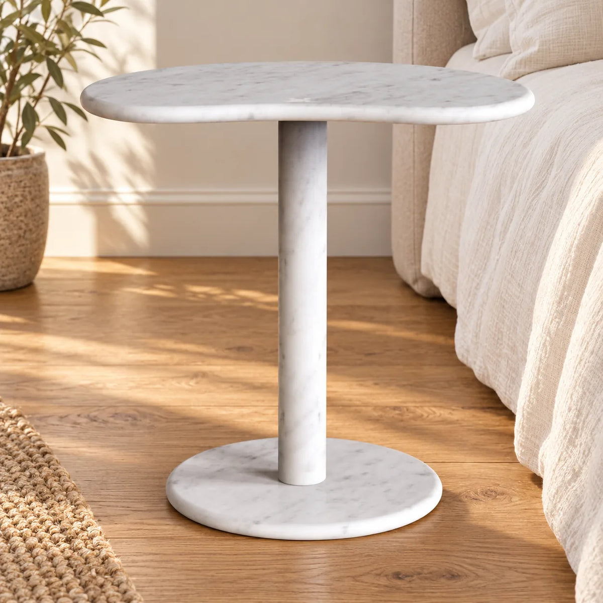 PeaPod white Carrara marble side table beside a linen bed, shown from a low frontal view