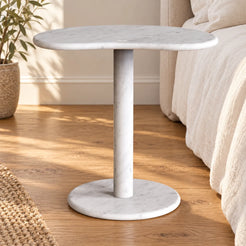 PeaPod white Carrara marble side table beside a linen bed, shown from a low frontal view