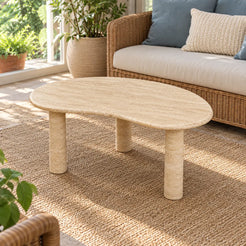 Elevated view of a single PeaPod Classico travertine coffee table in a garden-facing sunroom, showing its curved stone top and three cylindrical supports.