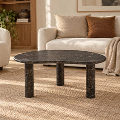 PeaPod Dark Emperador marble coffee table with a bean-shaped top and three cylindrical legs in a warm living room.