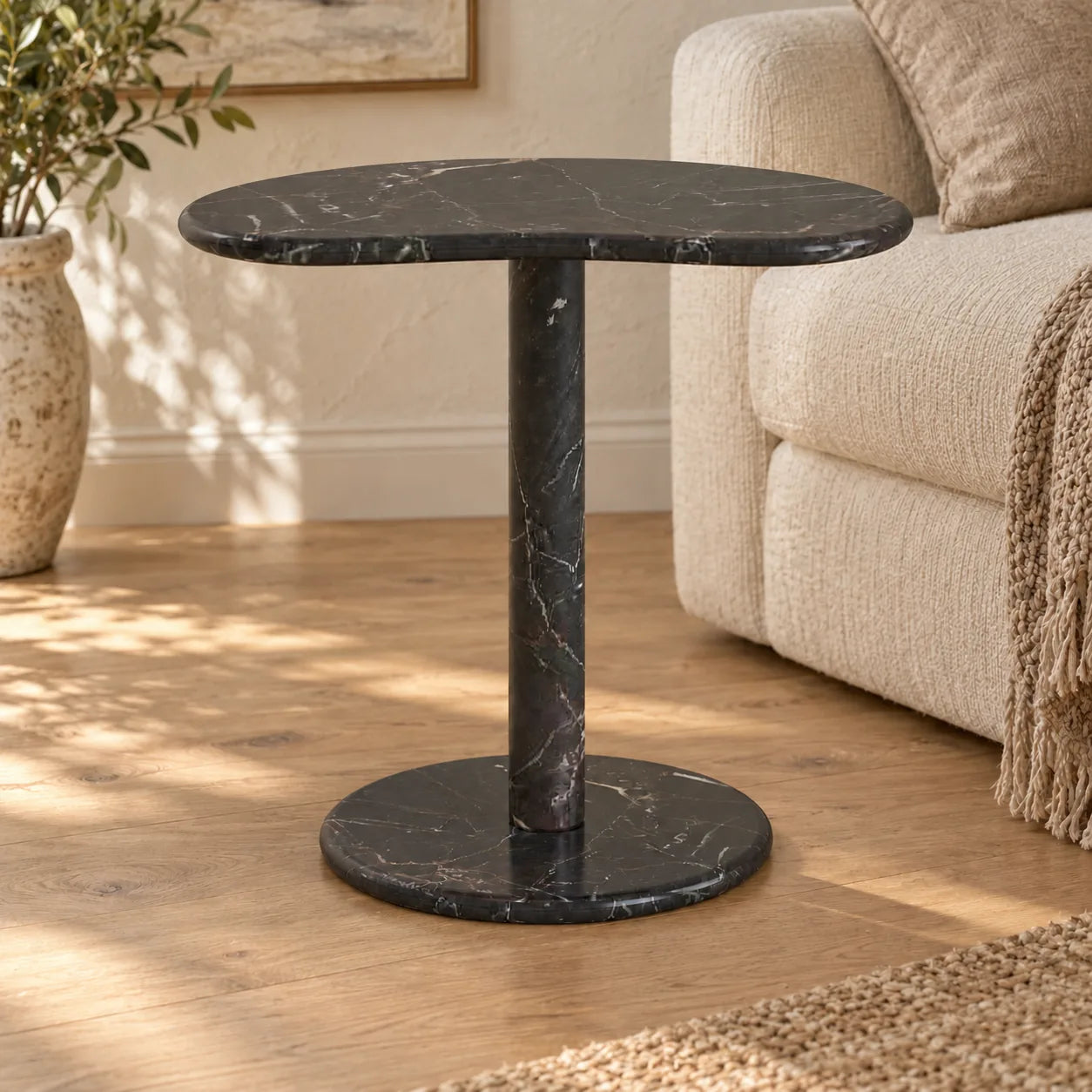 PeaPod Dark Emperador marble side table beside a cream sofa, shown from a low frontal view