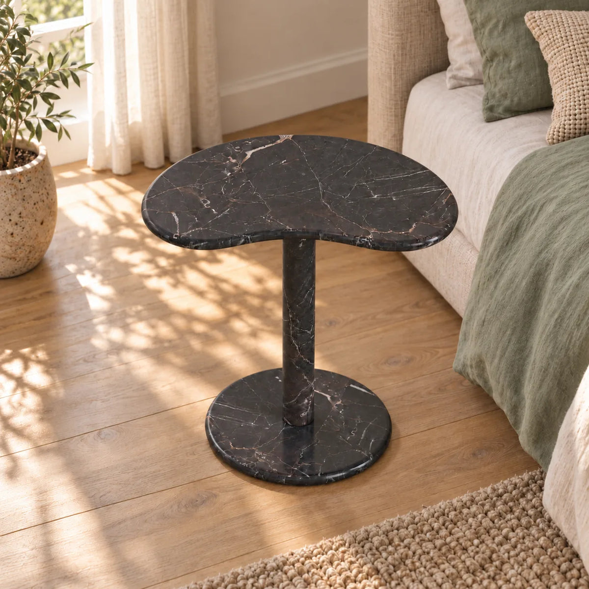 PeaPod Dark Emperador marble side table beside a linen bed, shown from a moderately elevated view