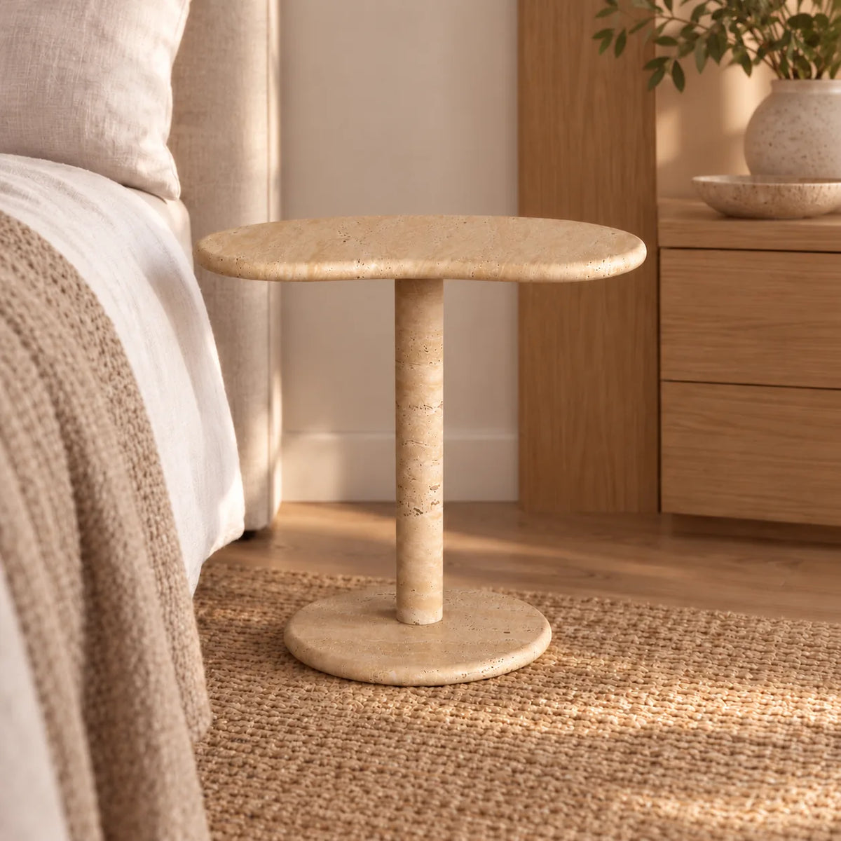 PeaPod beige travertine side table in a linen bedroom, viewed from a low angle