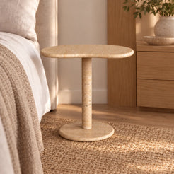 PeaPod beige travertine side table in a linen bedroom, viewed from a low angle