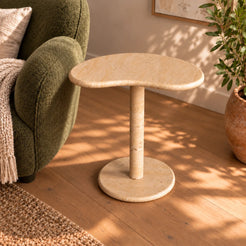 PeaPod beige travertine side table beside a reading chair, viewed at a moderate angle