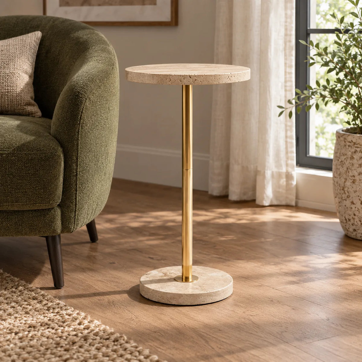 Pillar travertine-top side table with a gold-finish metal stand shown from a low angle in a reading corner.