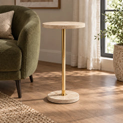 Pillar travertine-top side table with a gold-finish metal stand shown from a low angle in a reading corner.