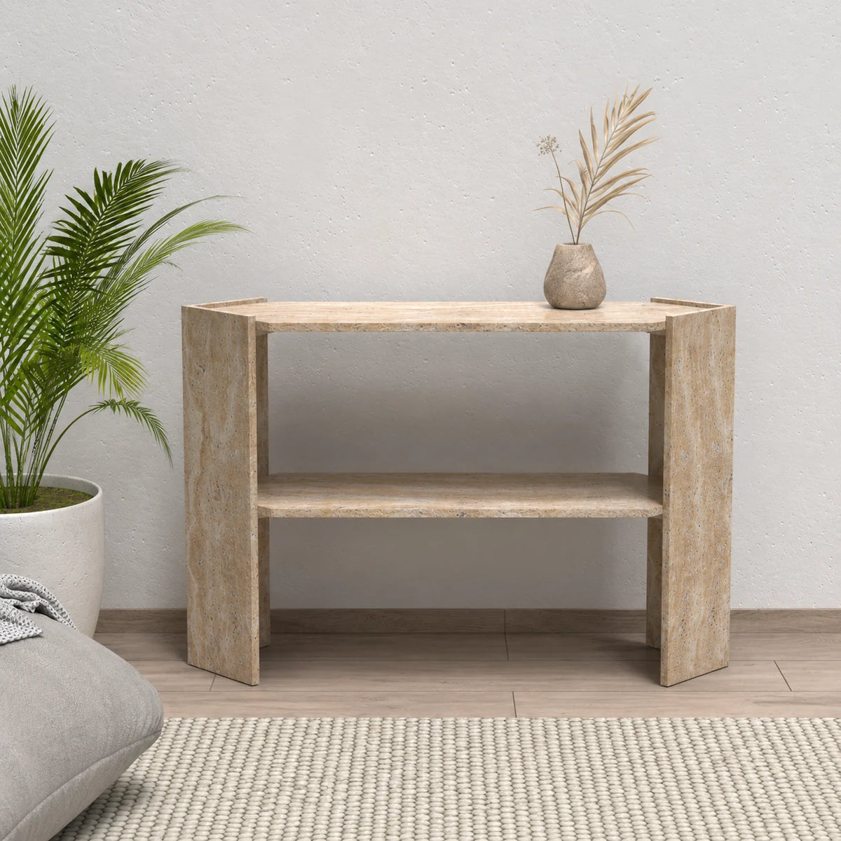 Front view of the Pomona beige travertine console table with its lower shelf beside a lounge chair in a natural living room