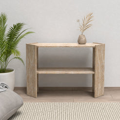 Front view of the Pomona beige travertine console table with its lower shelf beside a lounge chair in a natural living room