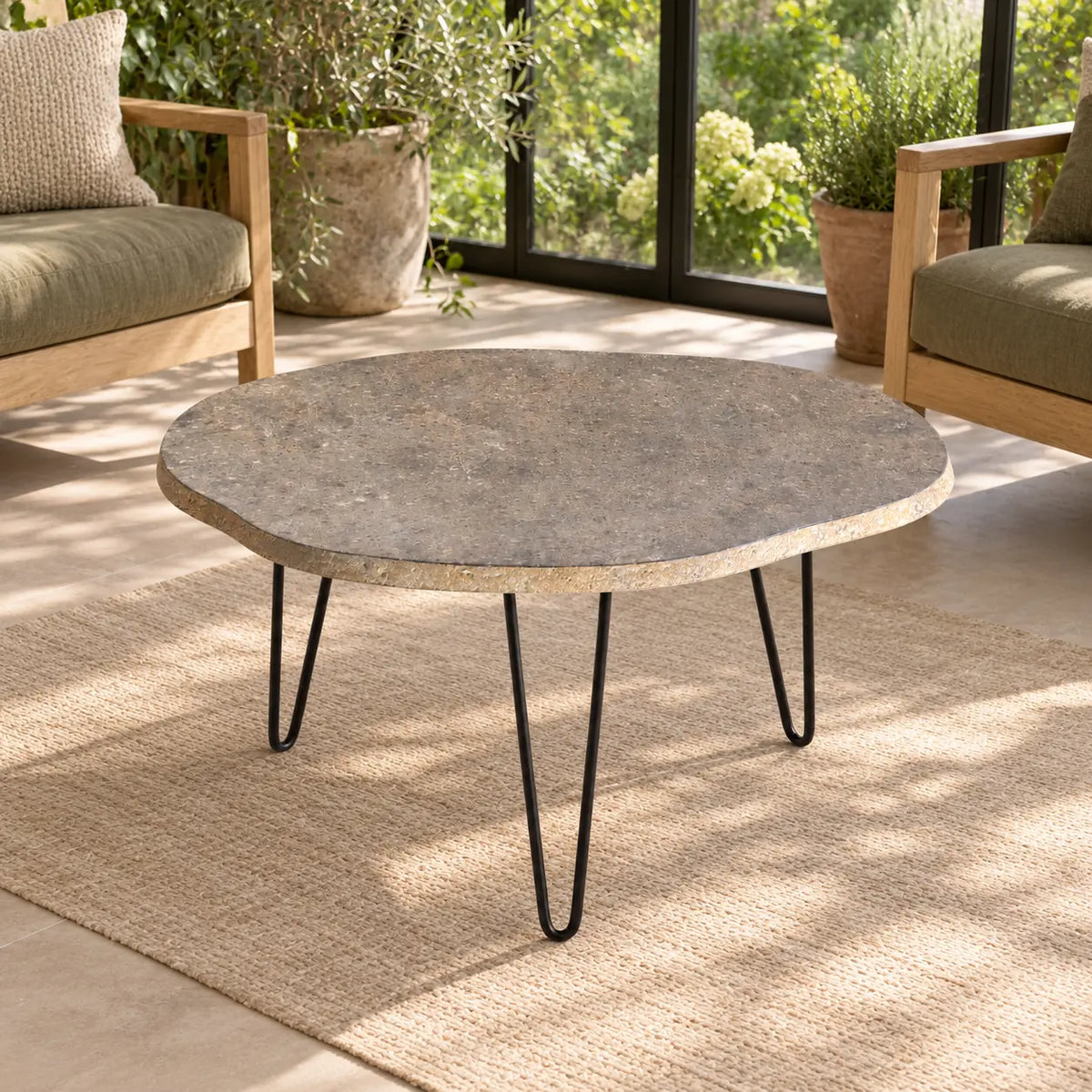 Elevated view of the RiverStone Yellow River Stone coffee table with an irregular stone top and three black hairpin legs in a garden-view sunroom