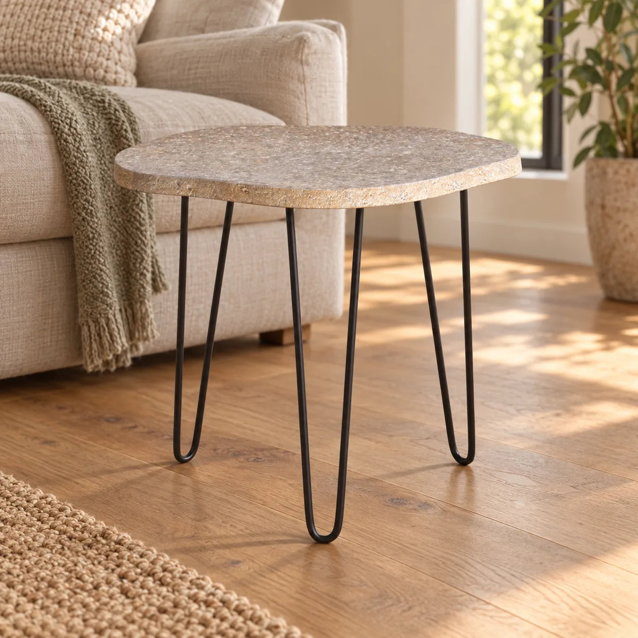 RiverStone Short natural river stone side table with three dark metal hairpin legs beside a linen sofa, shown from a low front view