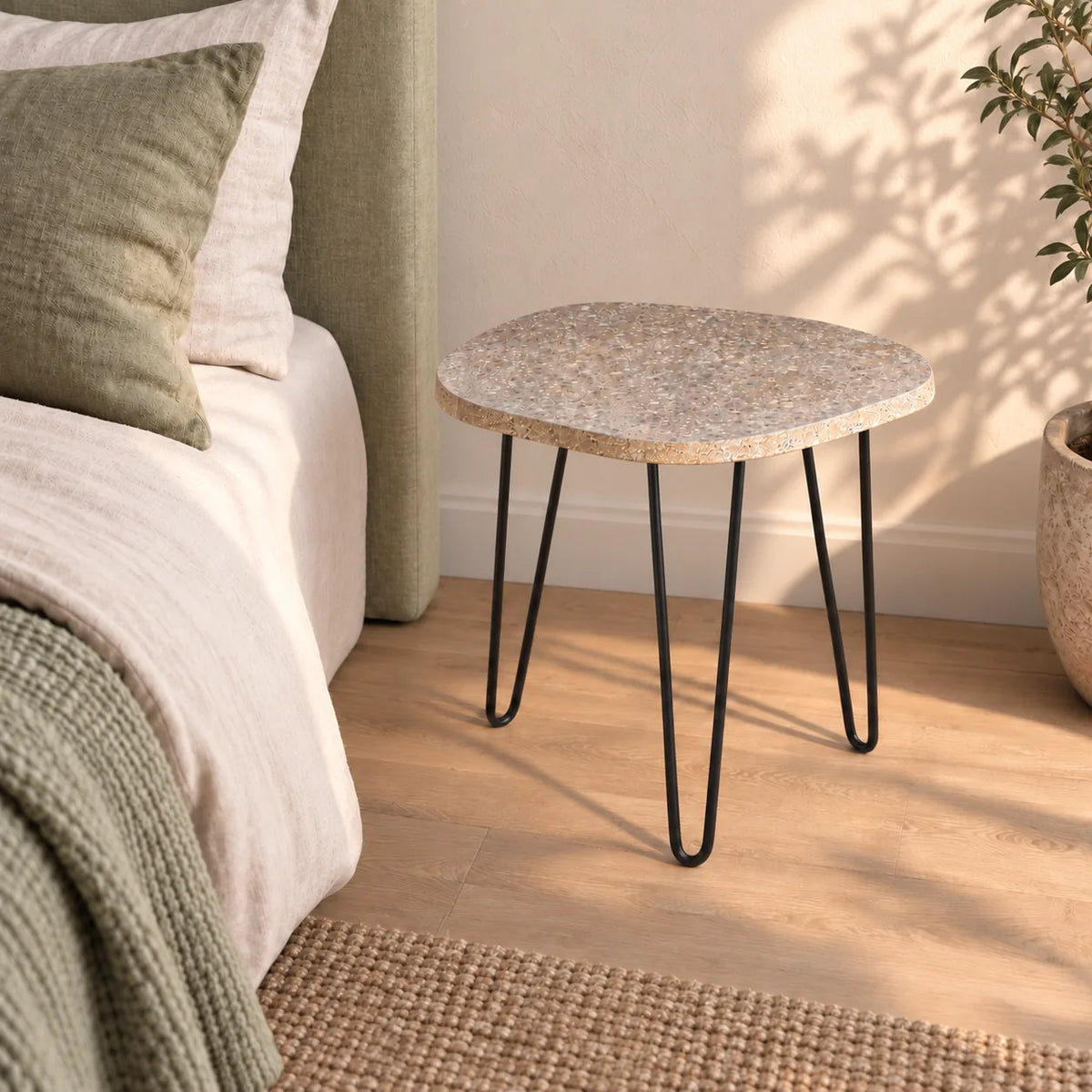 RiverStone Short natural river stone side table beside a sage linen bed, shown from an elevated right front view