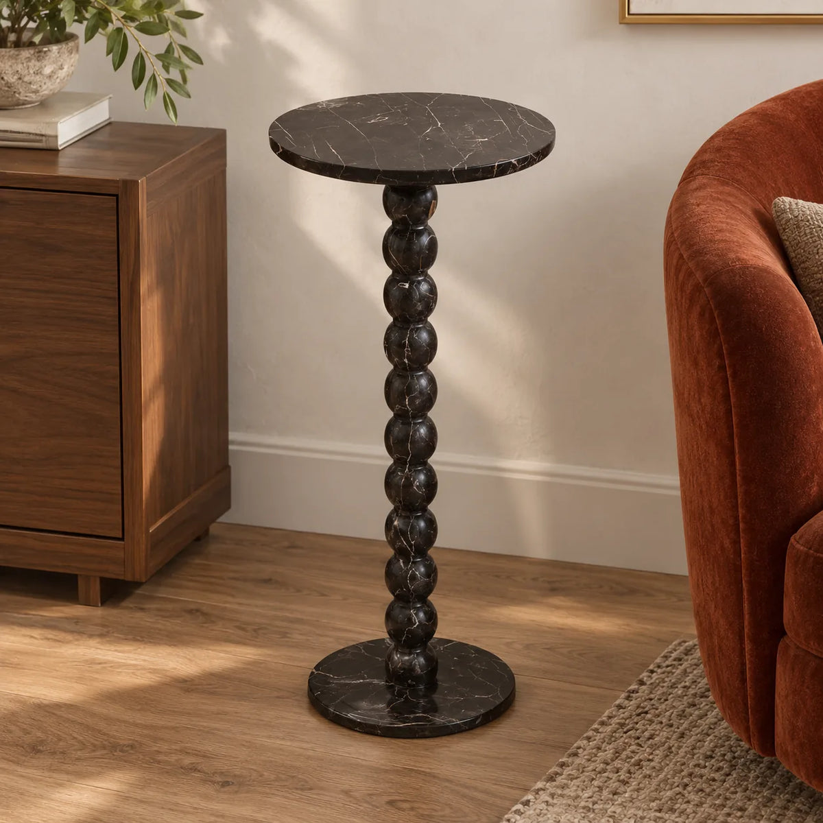 RoundBall Dark Emperador marble cocktail table beside a walnut cabinet and velvet chair, shown from a moderately elevated view