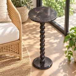 RoundBall Dark Emperador marble cocktail table beside a rattan chair in a sunroom, shown from a high front-quarter view