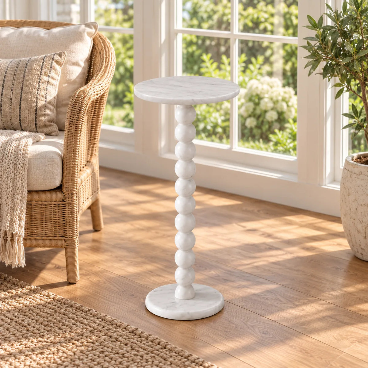 RoundBall Carrara marble cocktail table beside a rattan chair in a sunroom, shown from a moderately elevated front-quarter view