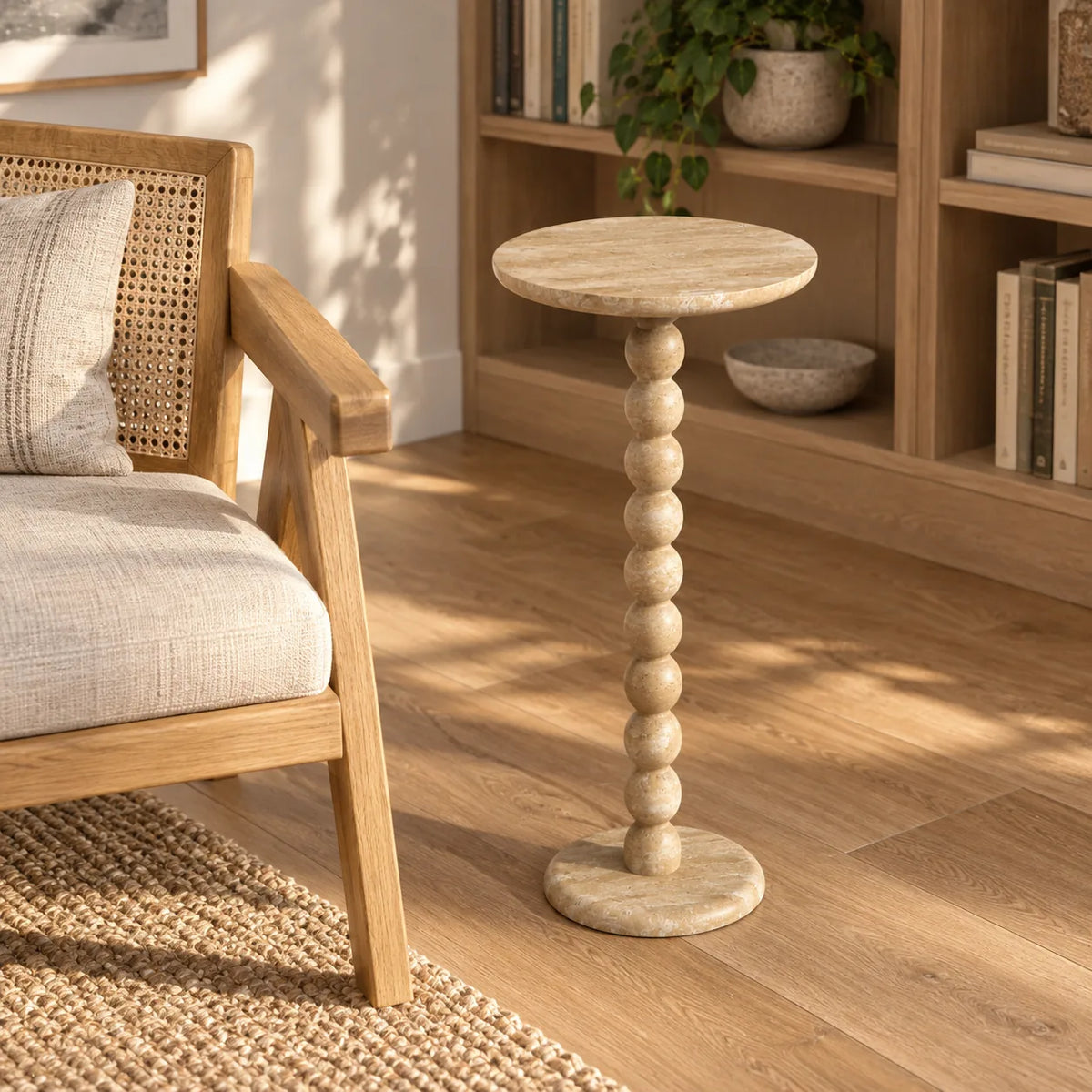 RoundBall Classico travertine cocktail table beside an oak chair in a library, shown from a moderately elevated front-quarter view