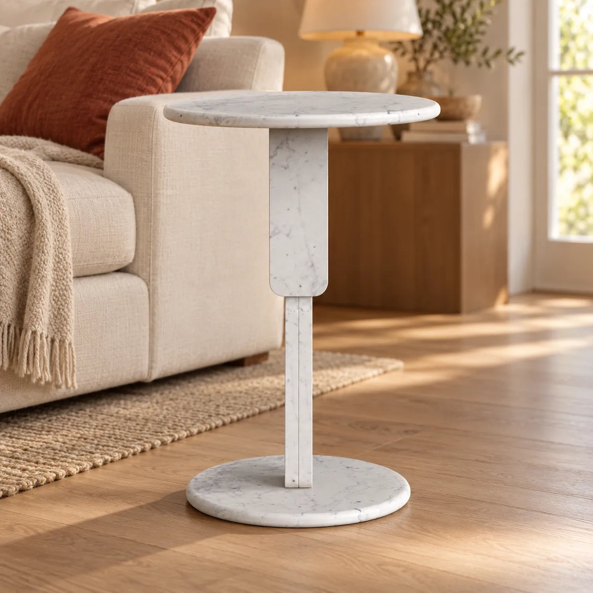 RoundGeo Carrara marble side table beside a linen sofa in a warm living room, shown from a low front view