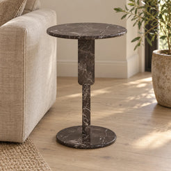 RoundGeo Dark Emperador marble side table beside a linen sofa, shown from a low front view with its geometric support