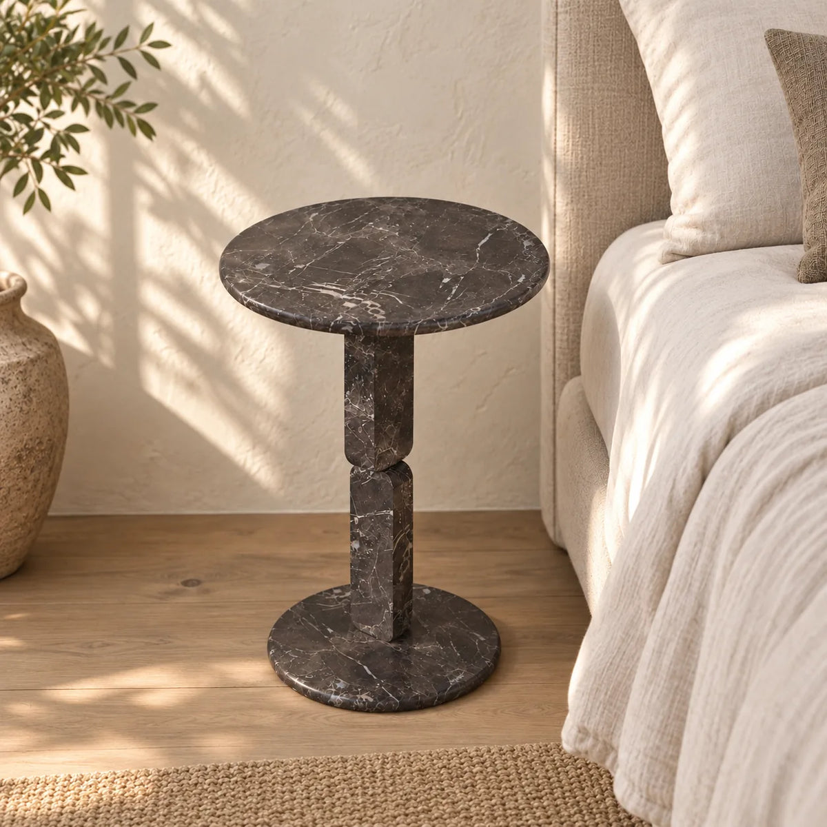 RoundGeo Dark Emperador marble side table beside a linen bed, shown from an elevated front-quarter view